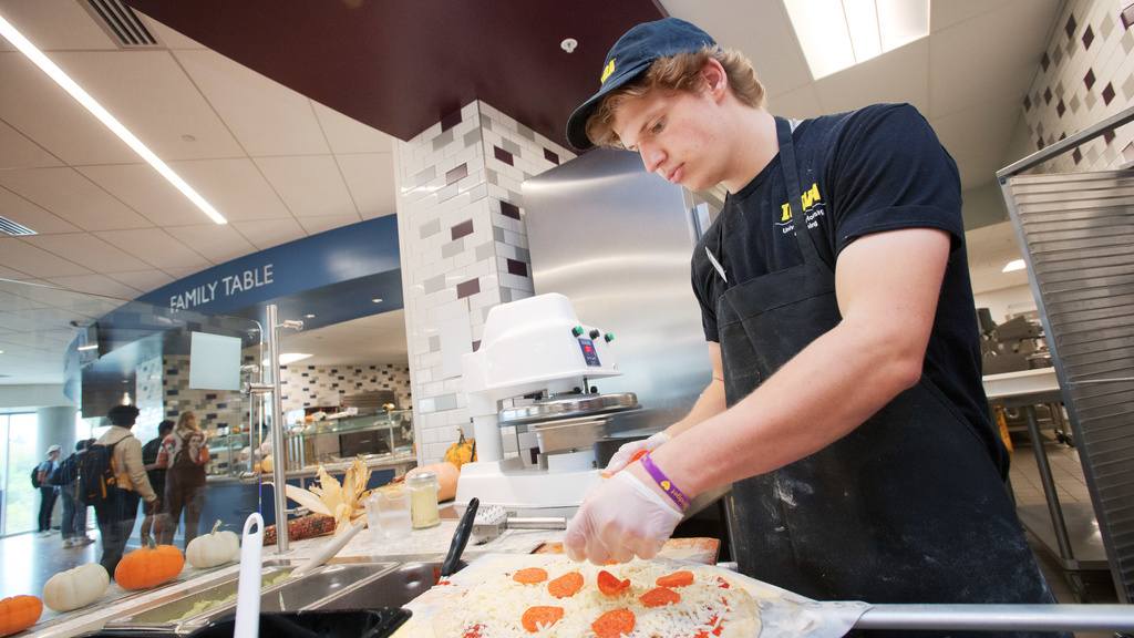 Student worker making pepperoni pizza